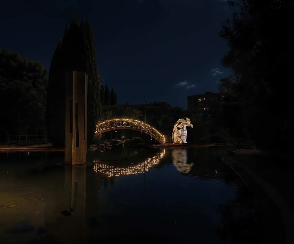 Rendering con l'AI: i pinguini di luminarie e il ponte illuminato che si specchiano nel laghetto del Parco 2 Giugno