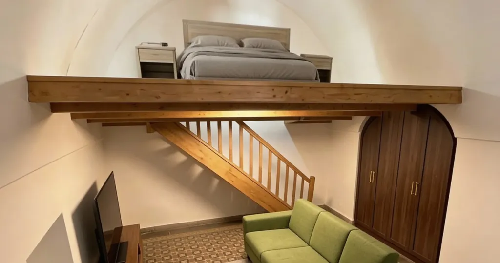Render con l'AI del soppalco in legno con il letto sotto la volta, la scala, il divano verde e l'armadio ad arco